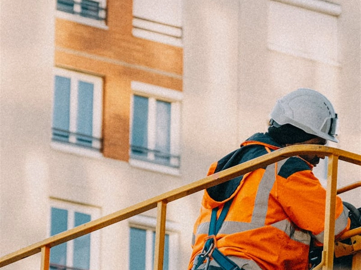 Werker met oranje hesje, helm en harnas op een hoogwerkerplatform