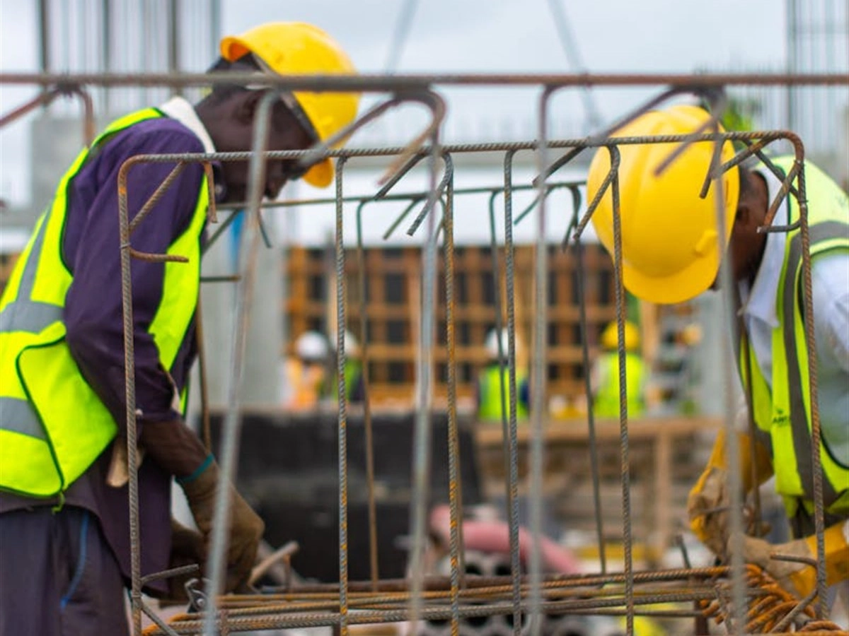 Twee bouwvakkers met gele helmen en fluorescerende hesjes bij wapeningsstaal op een bouwplaats